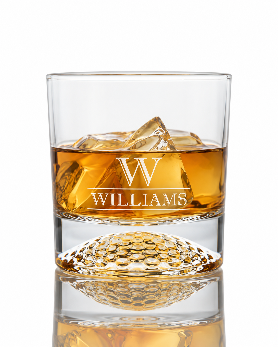 A clear whiskey tumbler glass with a golf ball shape base, filled with whiskey liquor and ice, on a white background with a reflection below. The front is engraved with a large letter W and the name WILLIAMS. Personalized Golf Ball Whiskey Glass Gift Set Engraved Golf Rocks Glass with Initials Kit Gifts for Golfers Tees Custom Golf Gift Set Box monogram