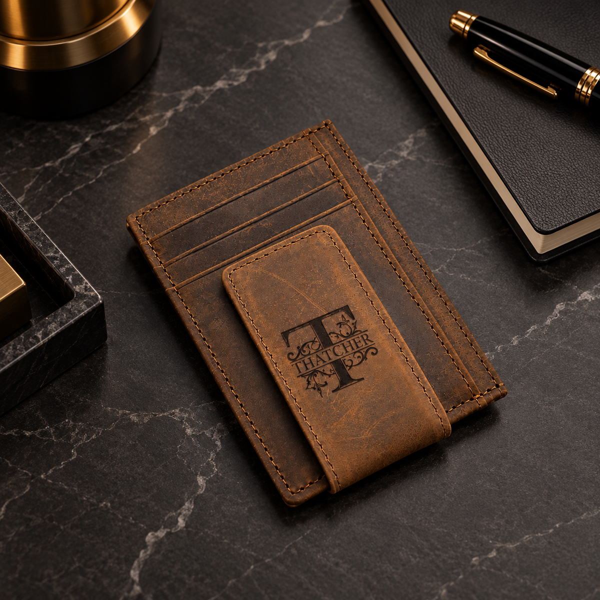 Custom engraved men's brown leather money clip wallet featuring a decorative Thatcher initial and name monogram. Slim minimalist cardholder with stitched leather details on an elegant black marble desktop.
