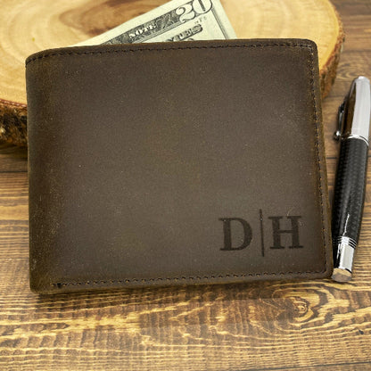 A hand holding a personalized brown leather bifold wallet with an open flap displaying multiple card slots and an ID window. There is text engraved on the wallet.